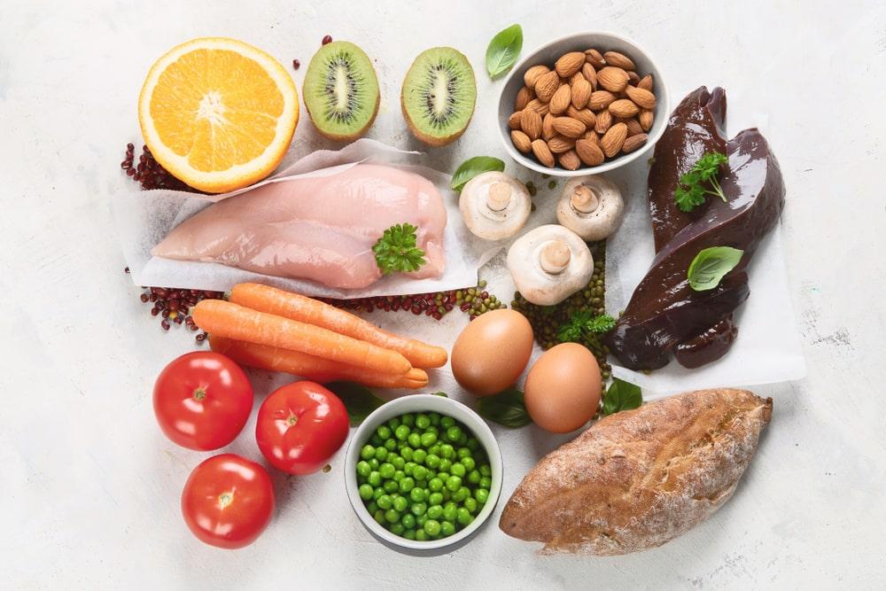 A table of kiwi, almonds, chicken, carrots, tomatoes, green beans and mushrooms