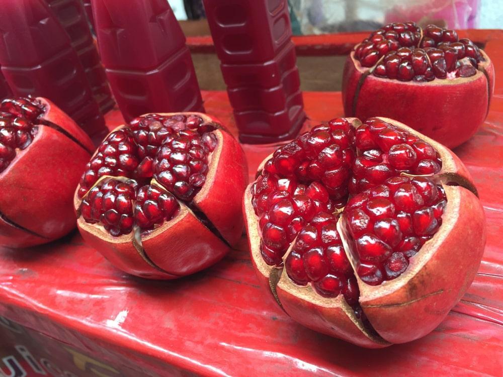 A Group of Opened Pomegranates Near Pomegranate Juice on a Red Surface