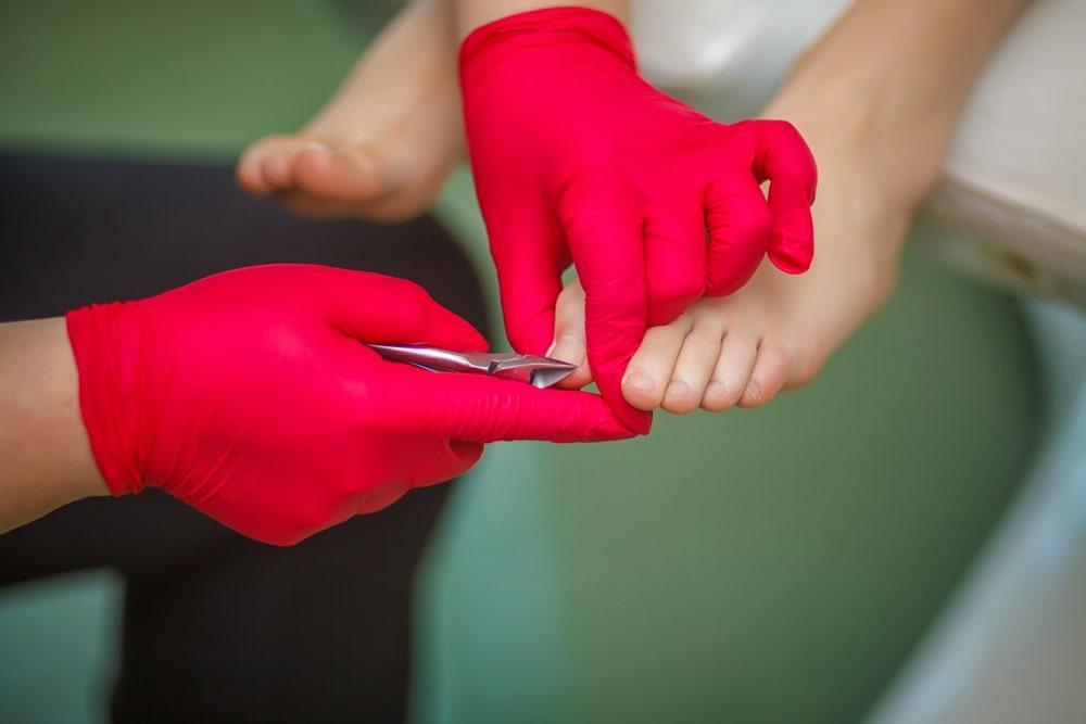 Hands with red gloves cutting toenails