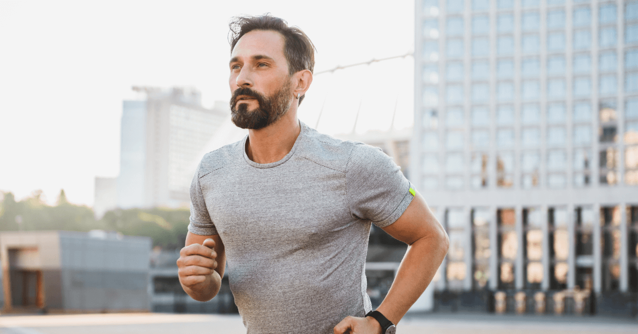 Image of handsome strong mature sportsman running at the street outdoors looking aside