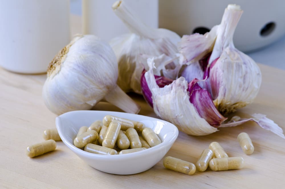 A Bowl of Garlic Pills Next to Garlic Bulbs