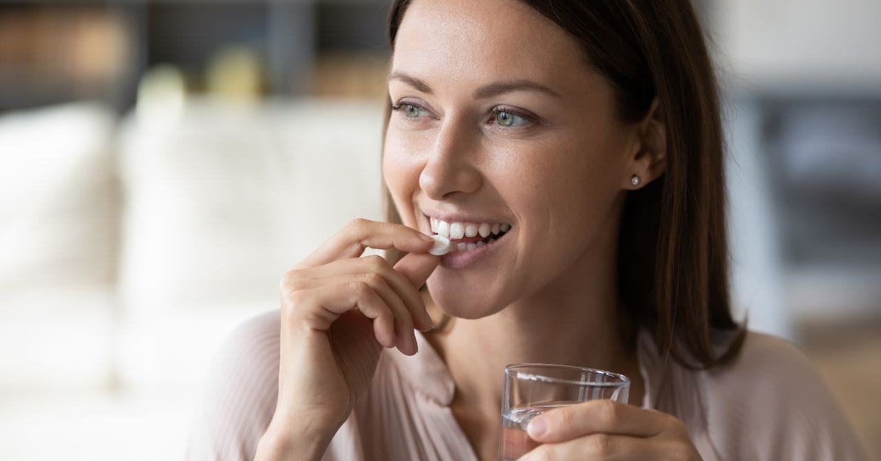 woman taking hormone balance supplements and holding a glass of water in her hand