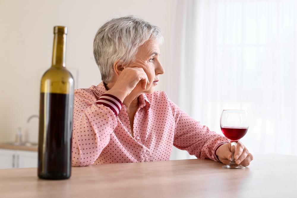 an elderly woman drinking red wine and looking through the window
