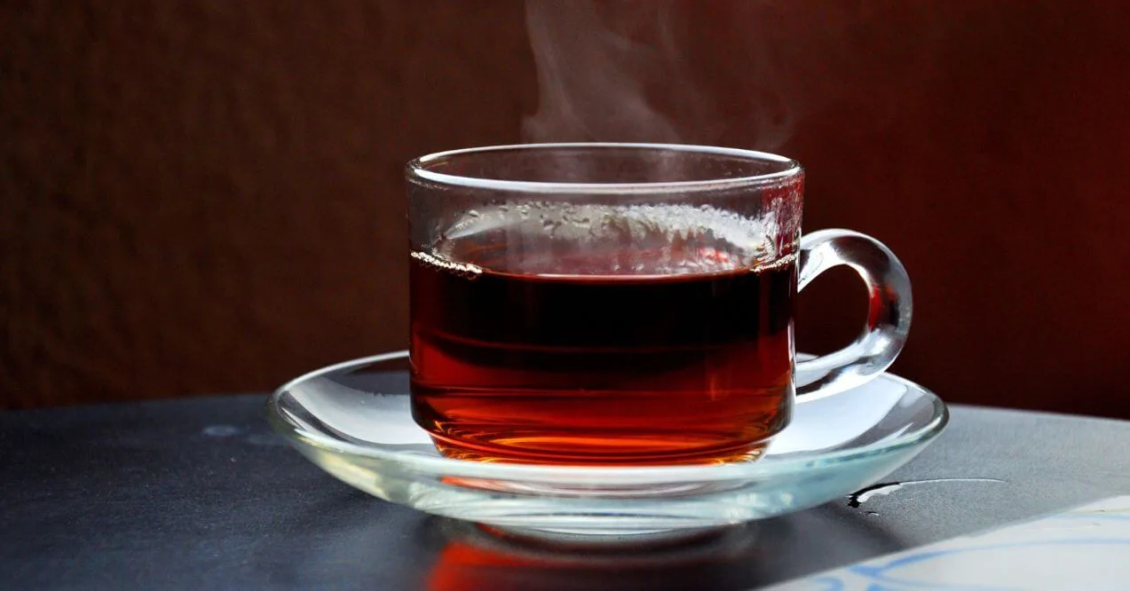 A steaming cup of black tea in a glass mug on a dark background.