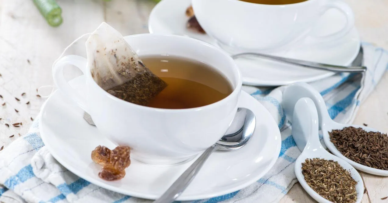 A white teacup with caraway tea, a tea bag, and caraway seeds in small spoons.