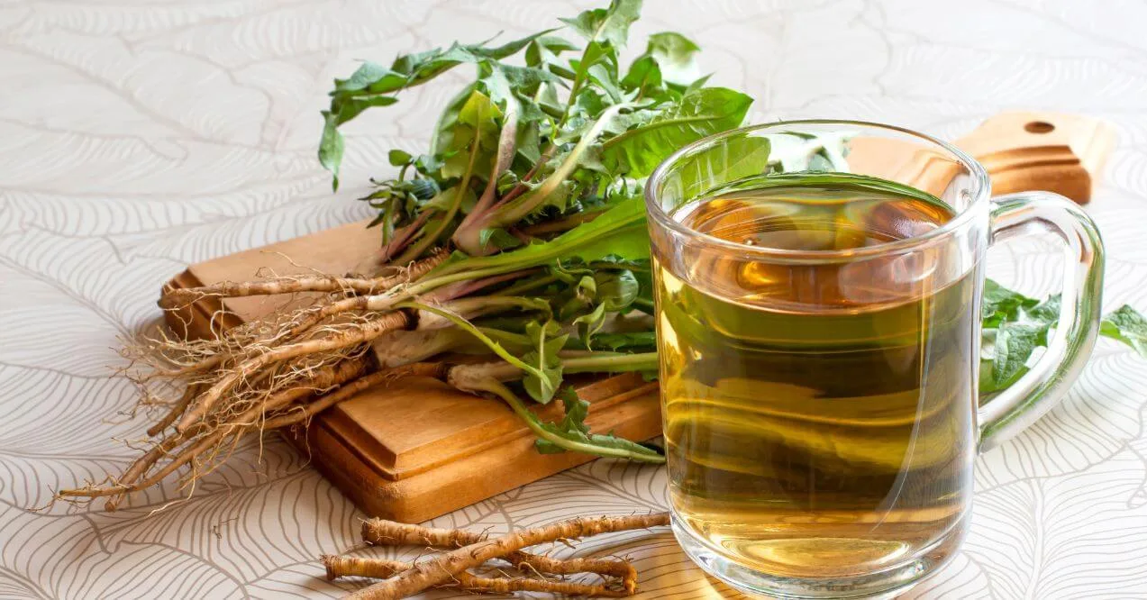 A glass mug of dandelion root tea with fresh dandelion roots on a wooden cutting board.