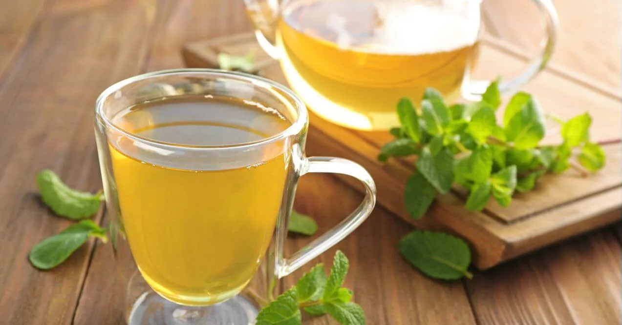 A glass cup of lemon balm tea with fresh green leaves on a wooden surface.