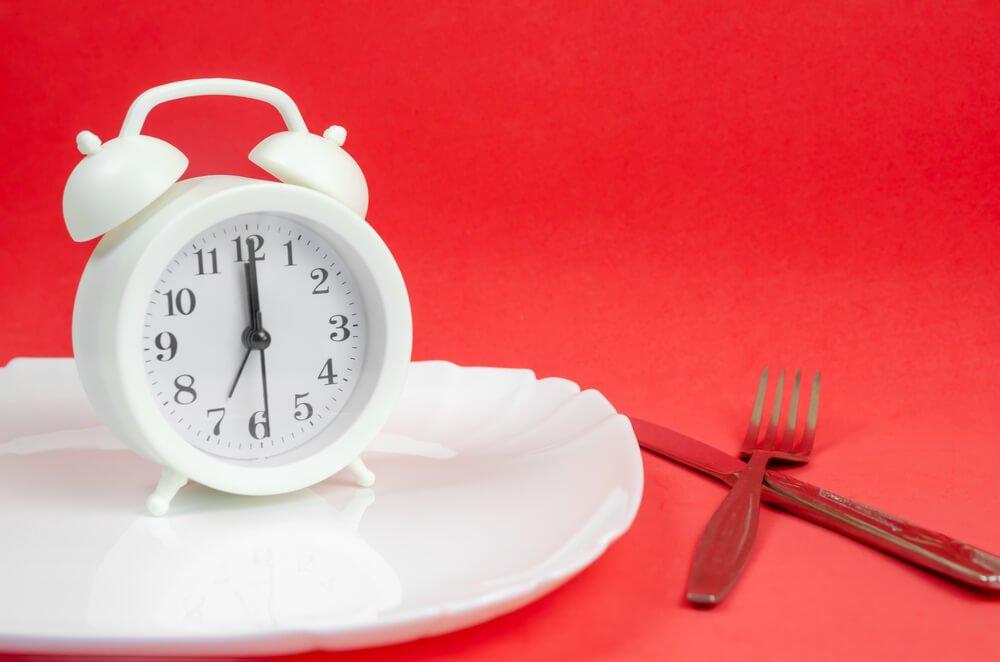 White clock on white empty plate next to cutlery red background