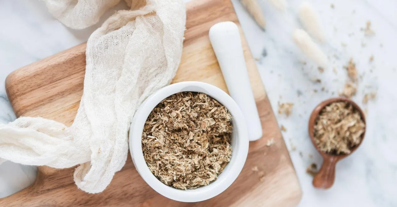 A white bowl of dried slippery elm bark on a wooden board with a mortar and pestle.