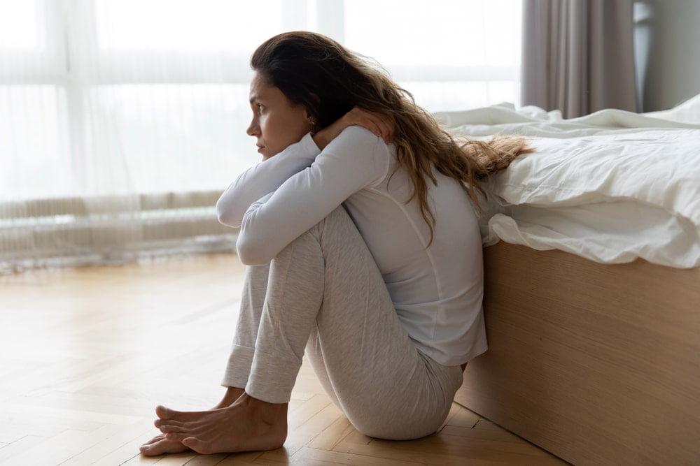 Unhappy Young Woman Sitting on the Floor Wrapping Her Arms Around Knees Wondering if UTIs Are Contagious