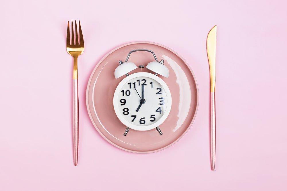 Retro Alarm Clock on Plate With Fork and Knife on Pink Background