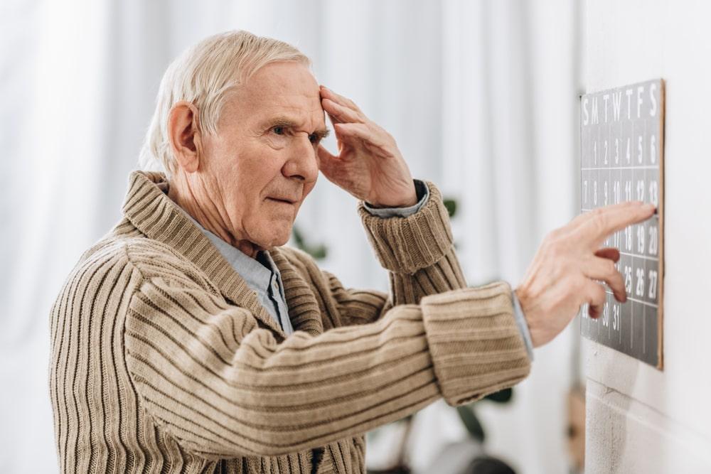 Senior Man Looking at Wall Calendar and Touching Head