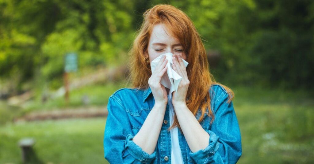 Young Woman Blowing Nose in Front of Blooming Tree