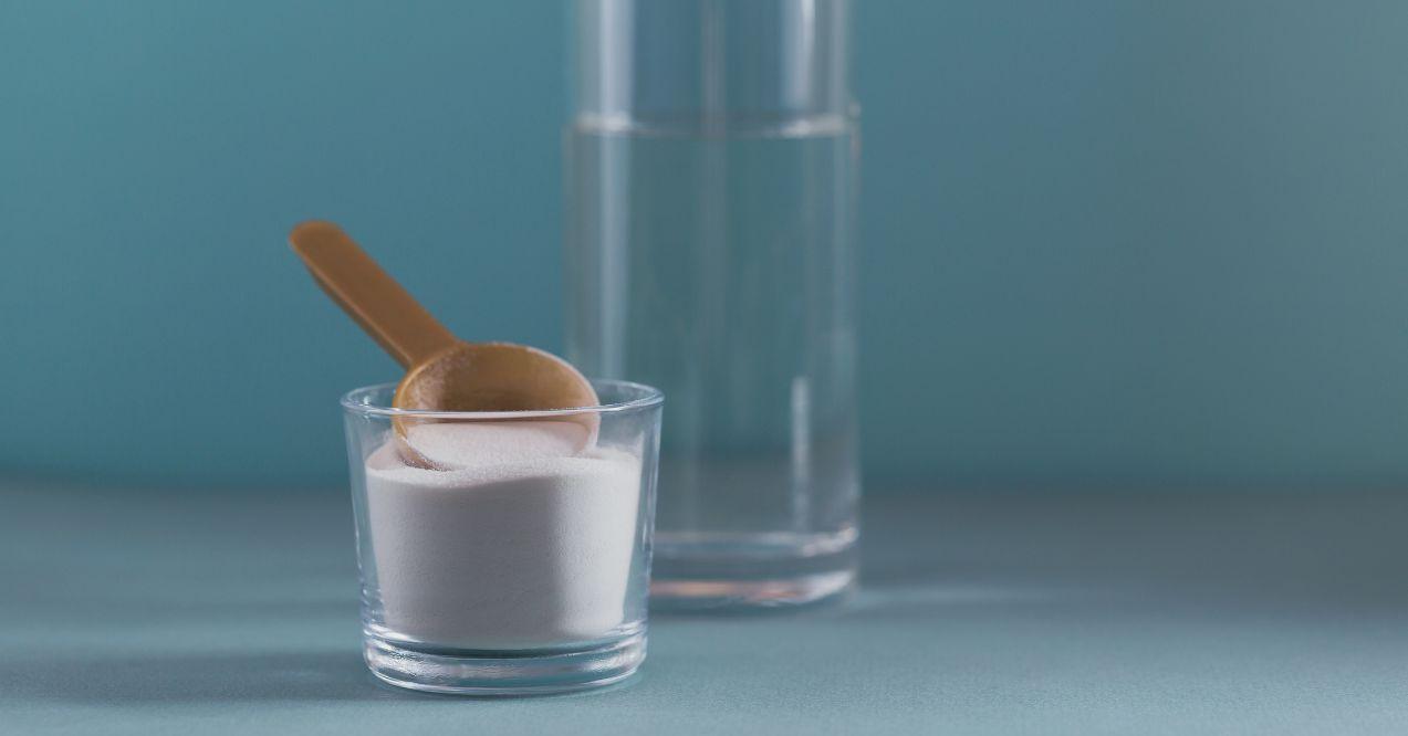 Glass with collagen dissolved in water and collagen protein powder on light blue background