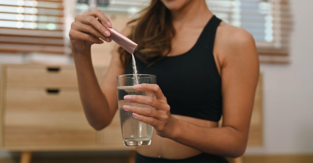 Young woman dissolving collagen powder in glass of water, preparing healthy supplement after exercise