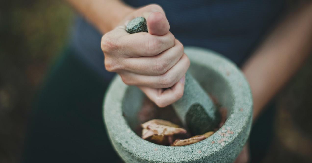 Person grinding herbs for thyroid health on mortar and pestle