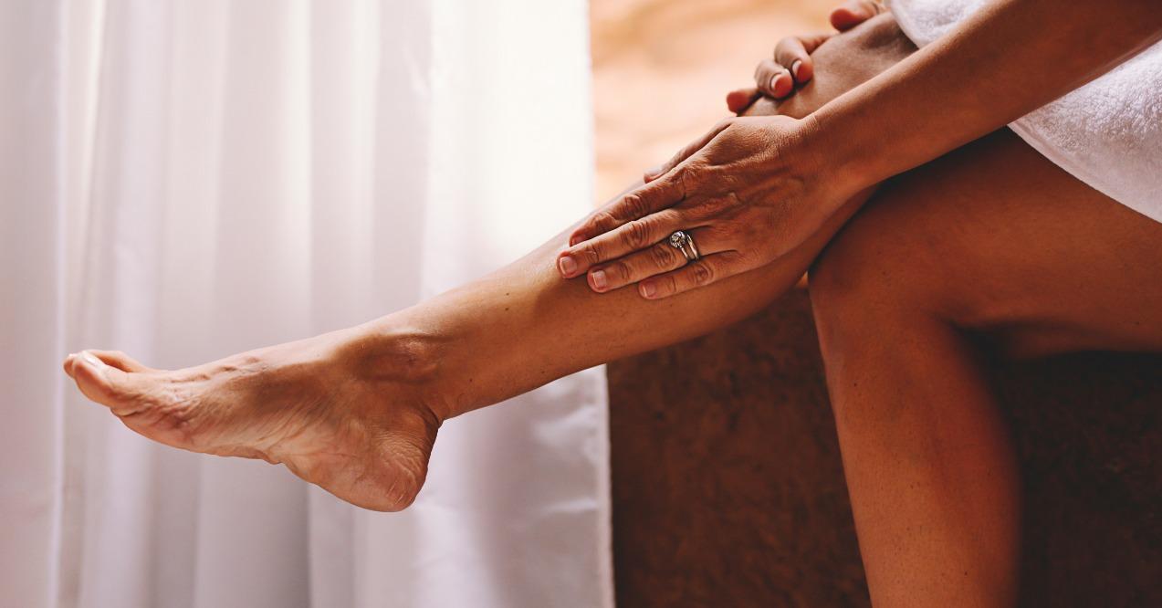 Adult lady applying skin care tanning cream on leg for spider veins coverage.