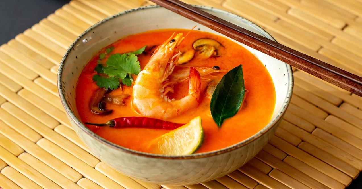 A bowl of tom yum soup with prawn and lime on a bamboo table zoomed