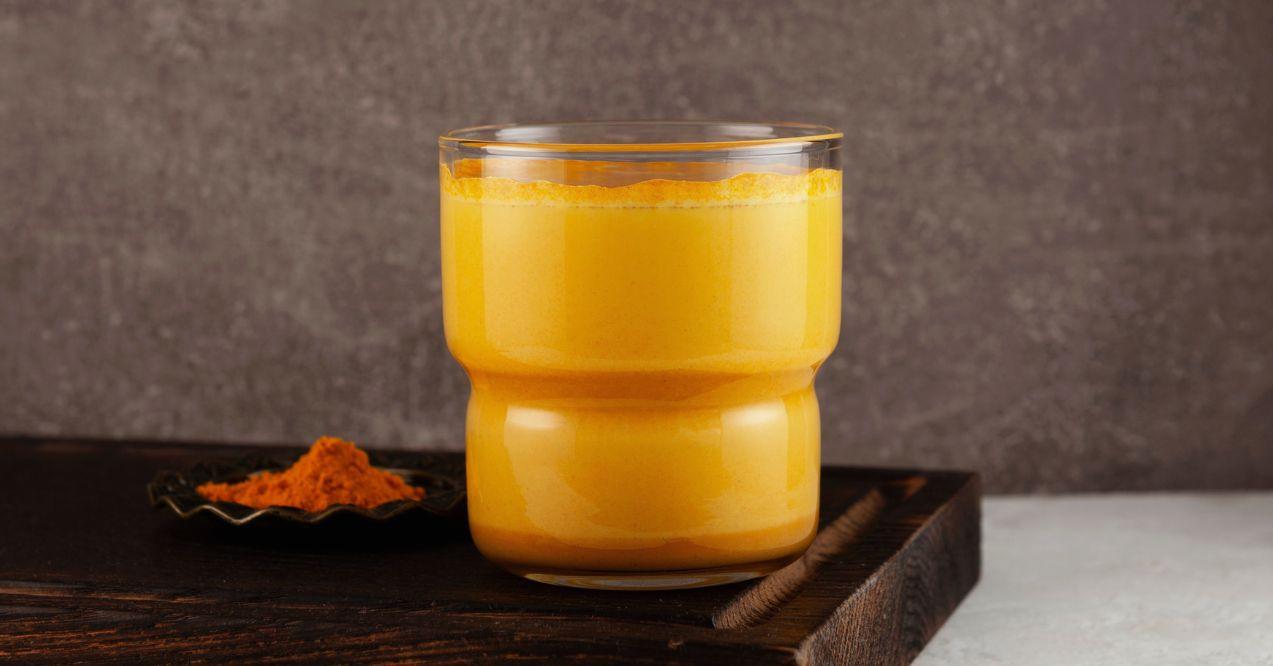 Yellow turmeric tea in a glass on wooden stand.