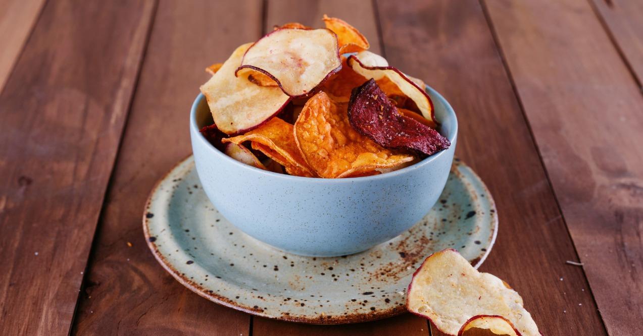 Healthy vegetable beetroot, sweet potato and white sweet potato chips in a blue cup closeup on a rustic wooden background