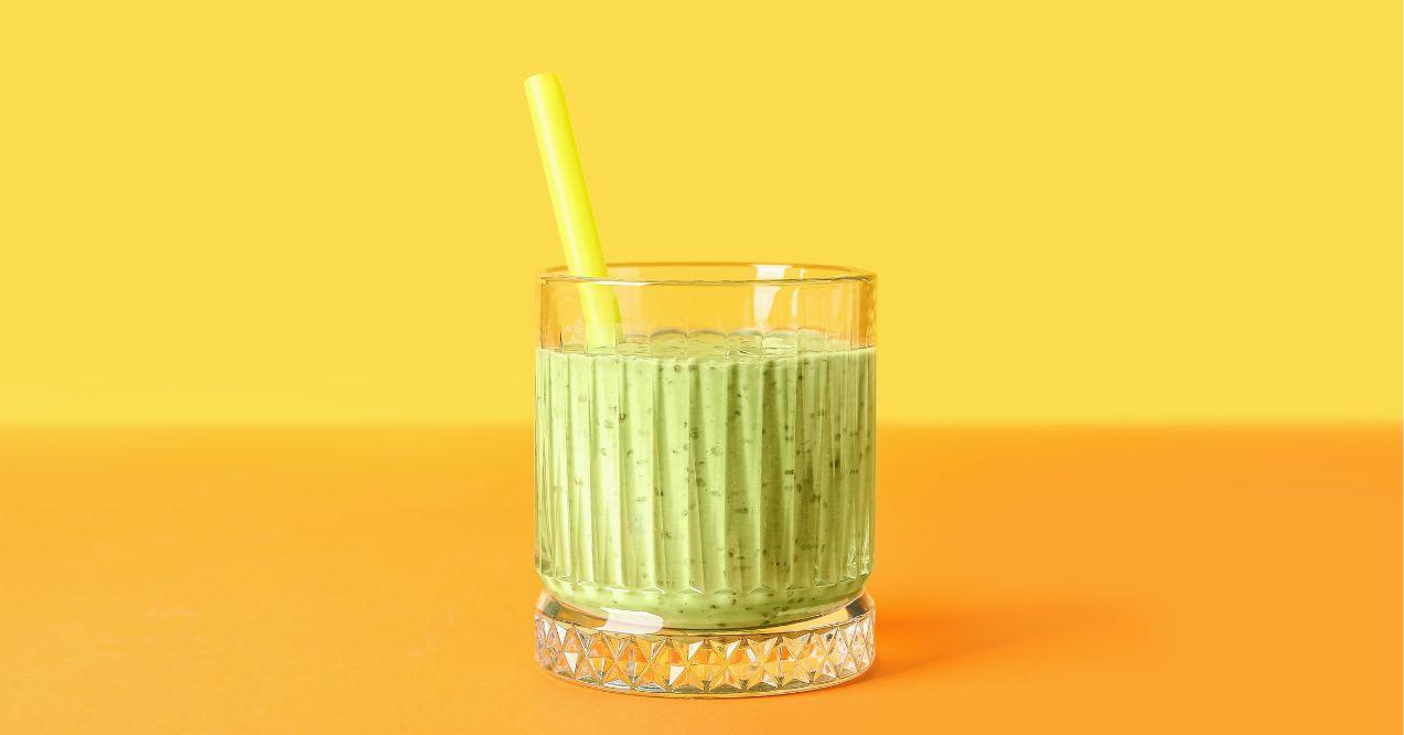A glass of detox green smoothie in a glass on a yellow color background.