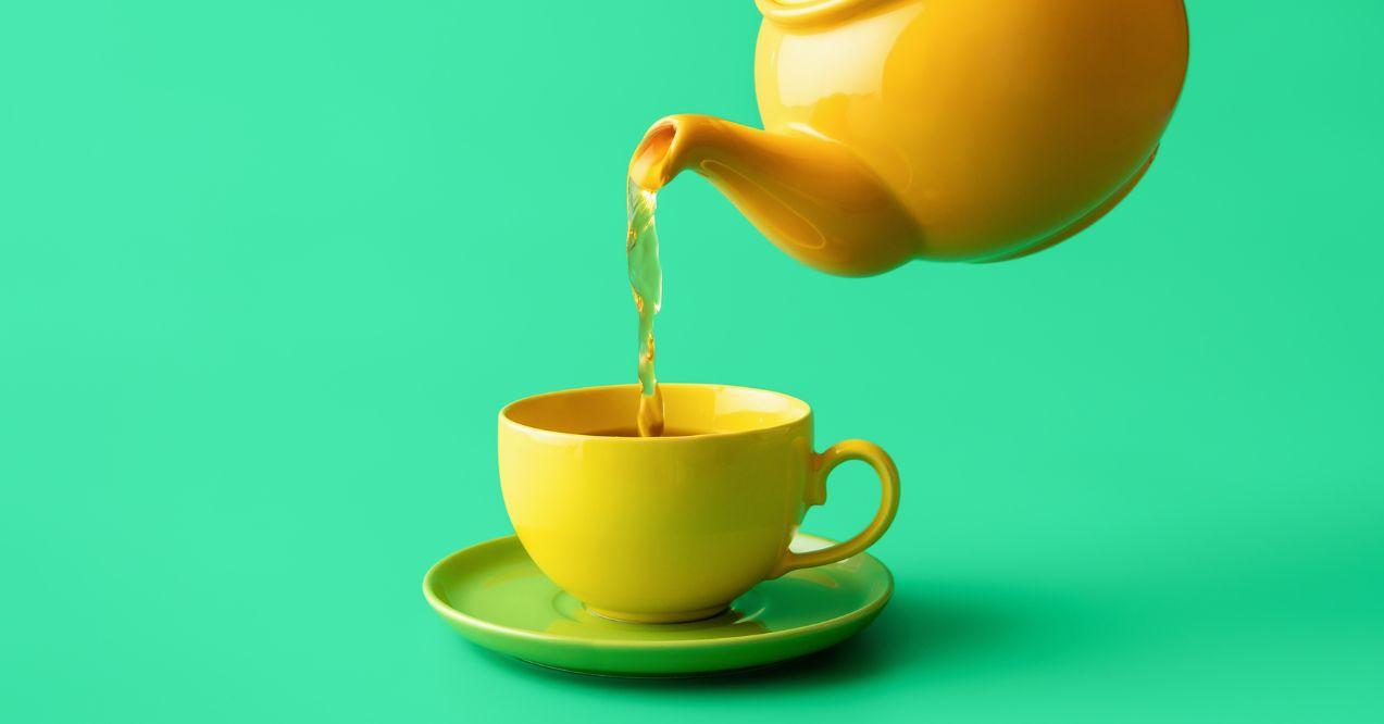 Yellow tea cup and tea pot on a green colour background. Pouring tea,