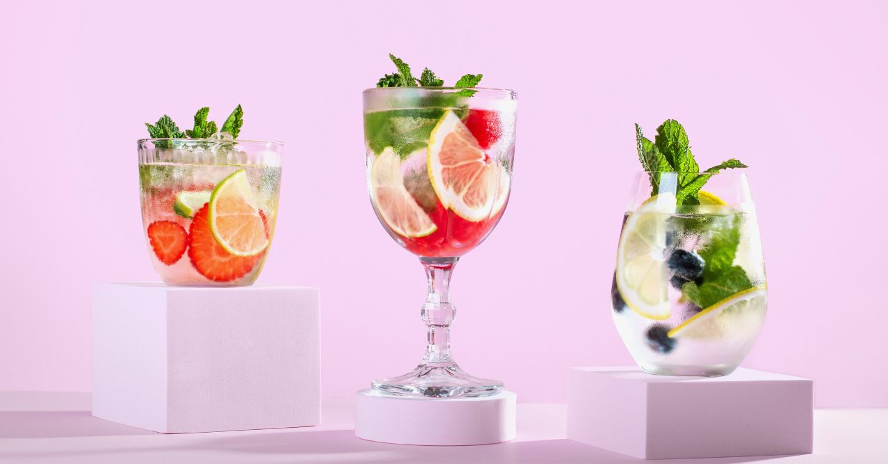 Three glasses of detox water with fruit on platform on purple color background.