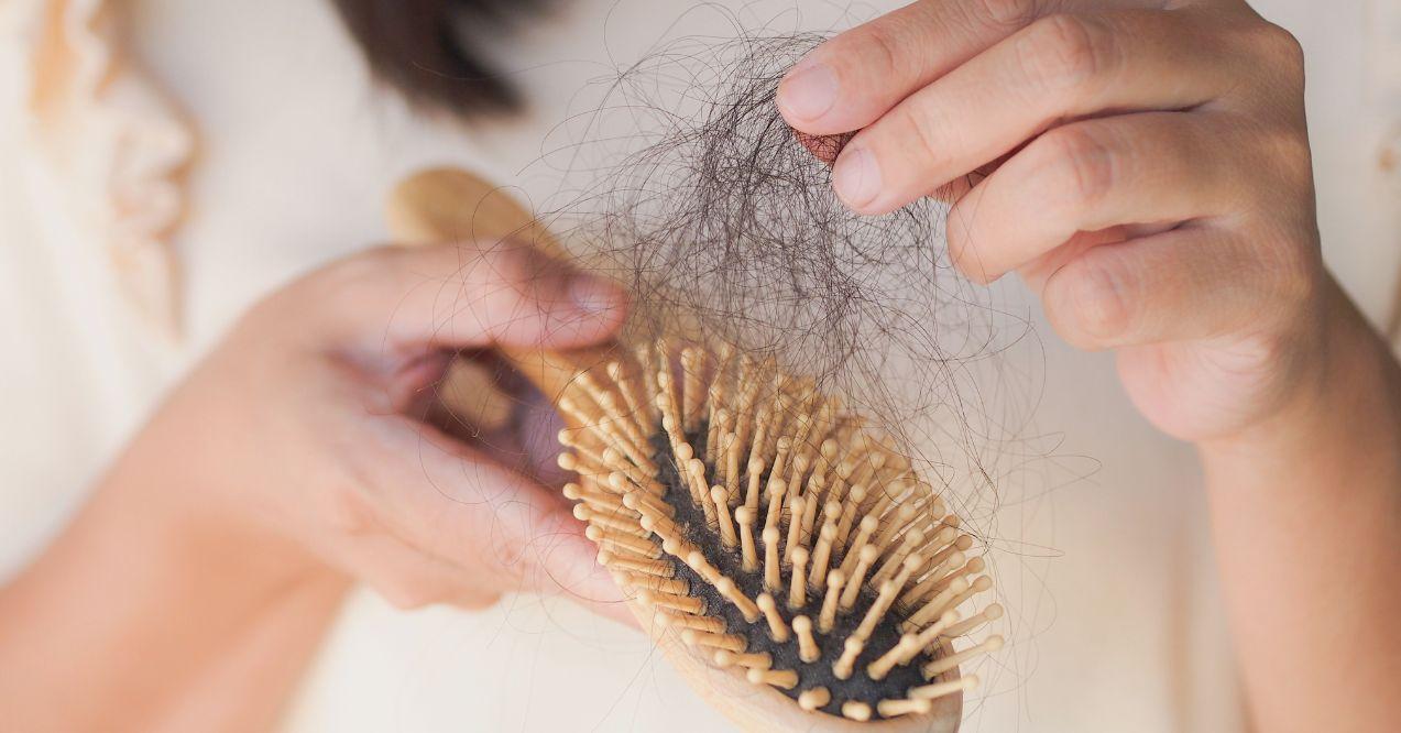 Woman hands taking out dark hair from a wooden hairbrush.