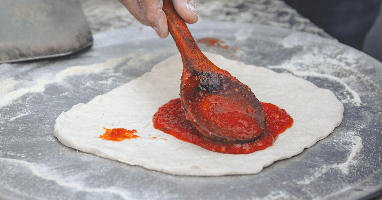 Tomato sauce being poured on a pizza dough.
