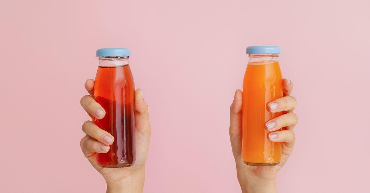 Two hands holding detox juice on a pink colour background.