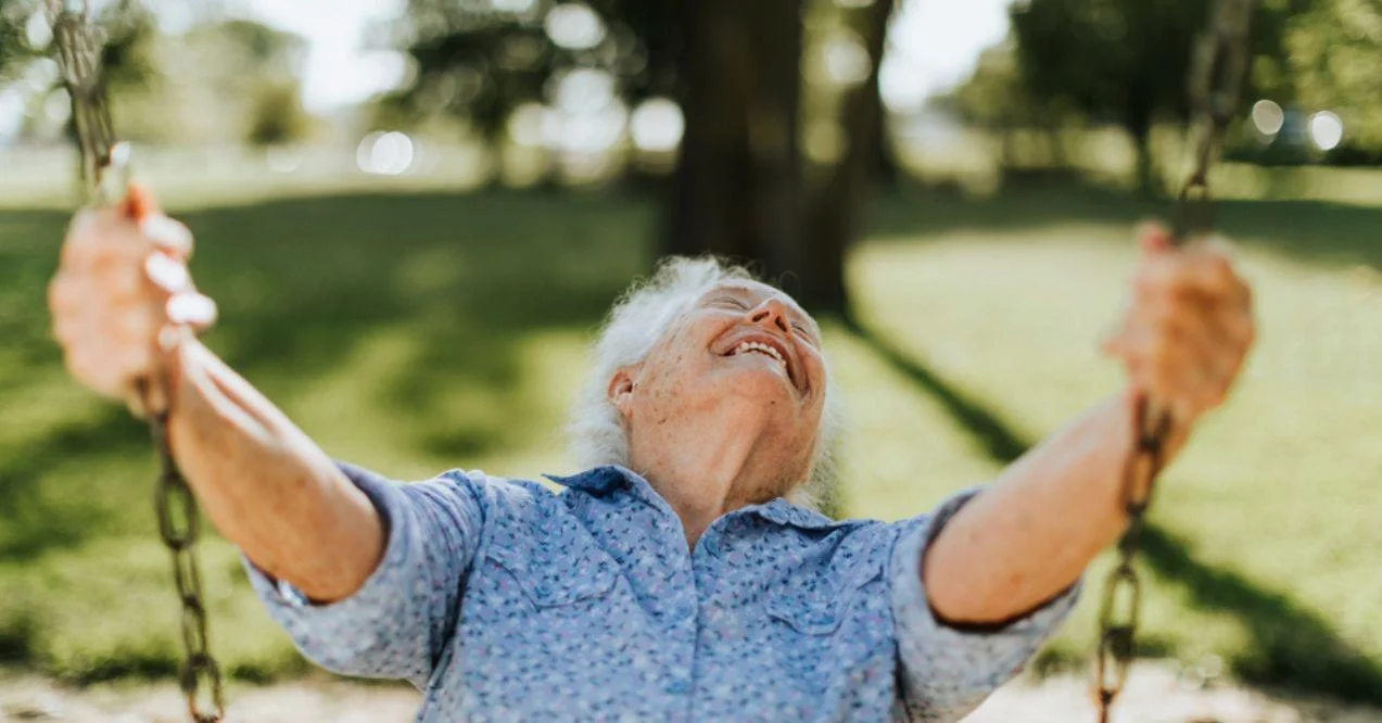 Cheerful senior woman on a swing at a playground