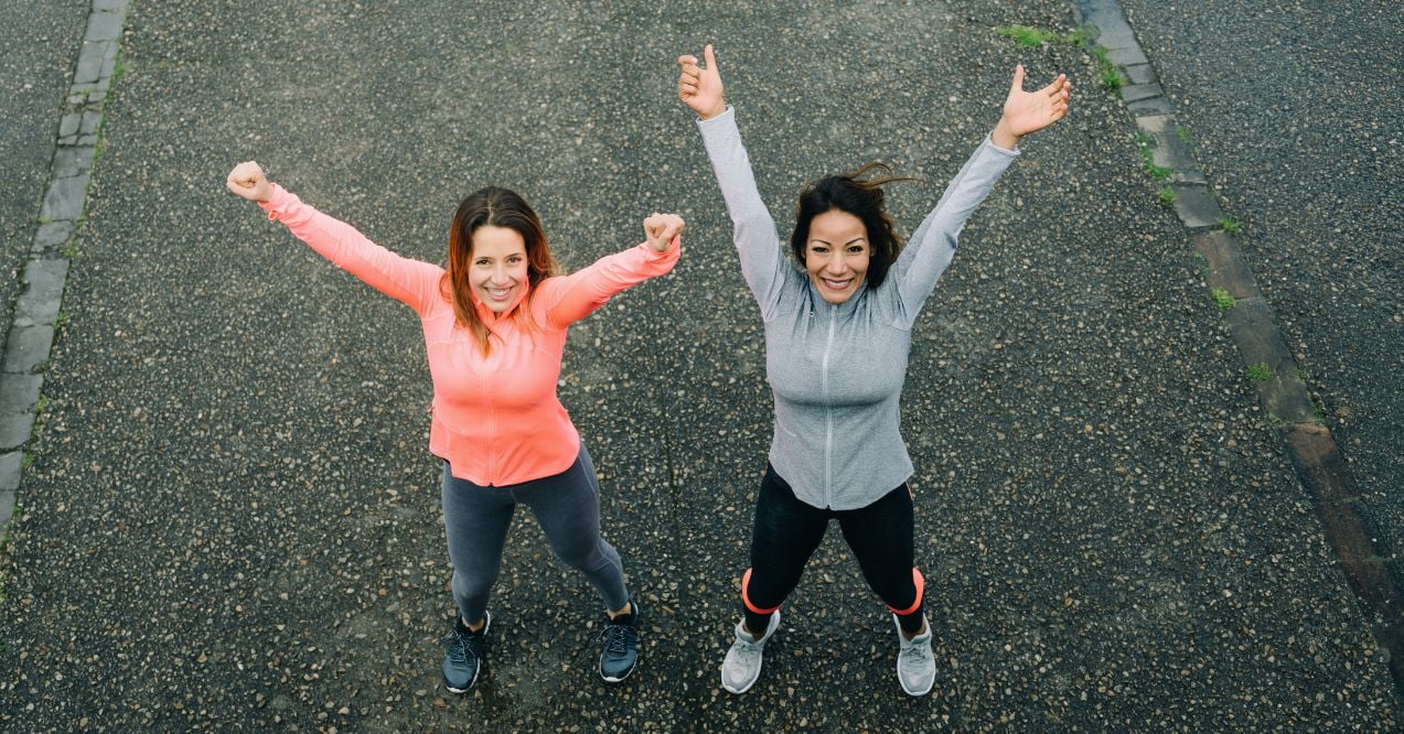 Two urban sporty women with arms up celebrating workout success.