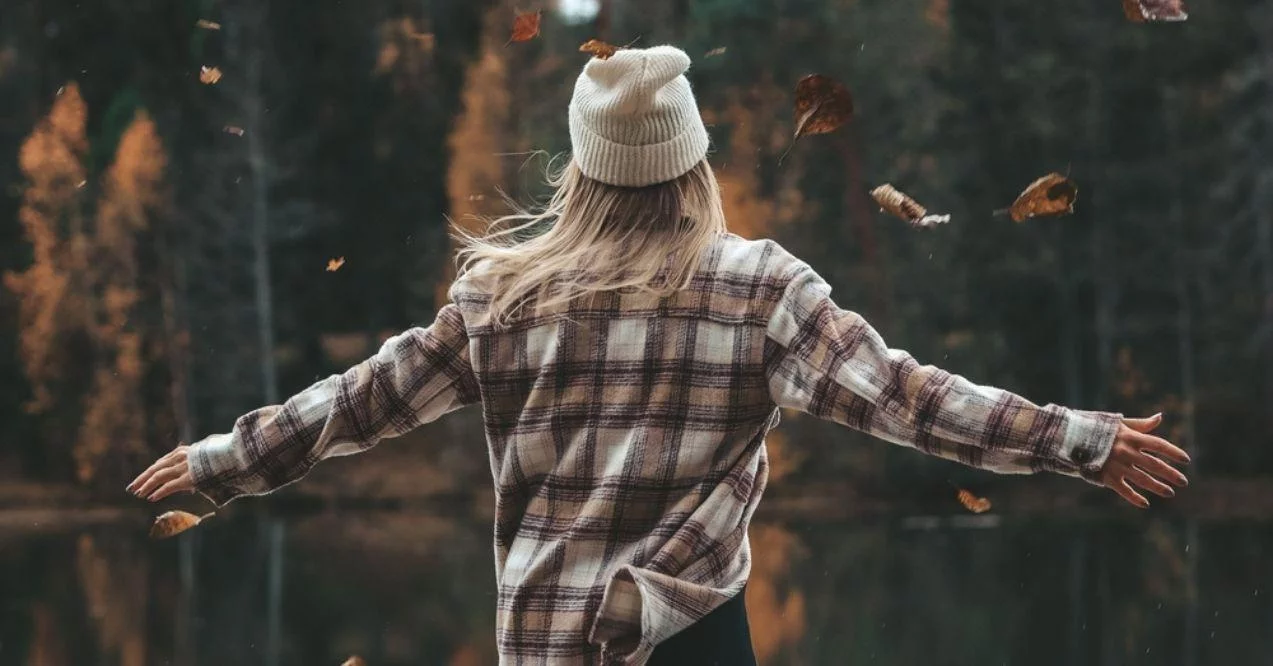 Young adult woman embracing autumn as leaves fall down