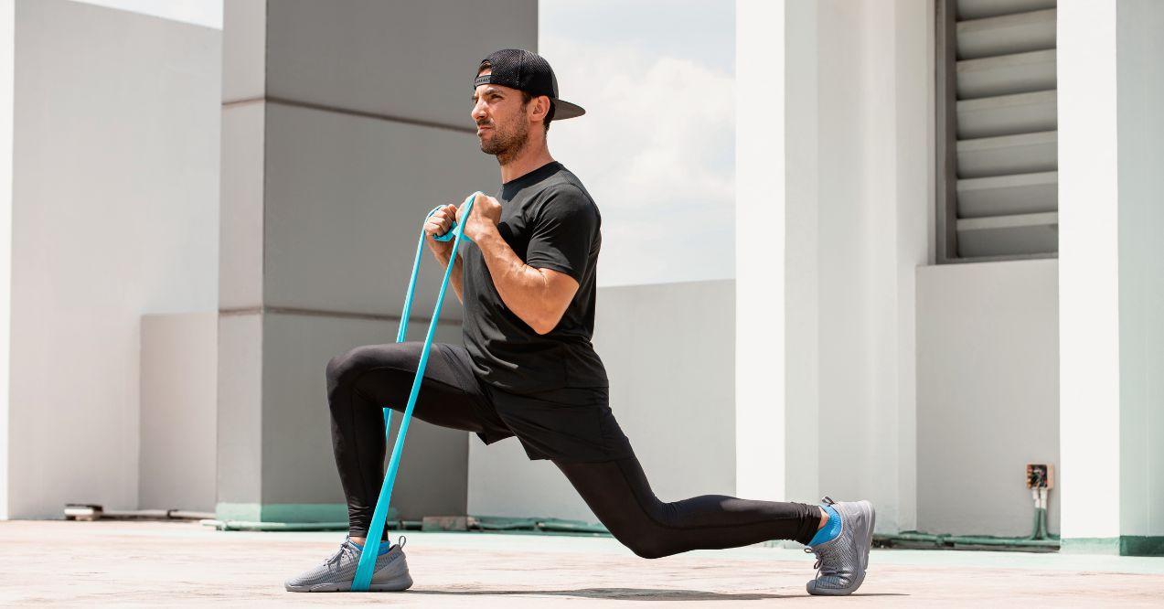 Handsome Latino sports man doing lunge workout with resistance band outdoors in the sun