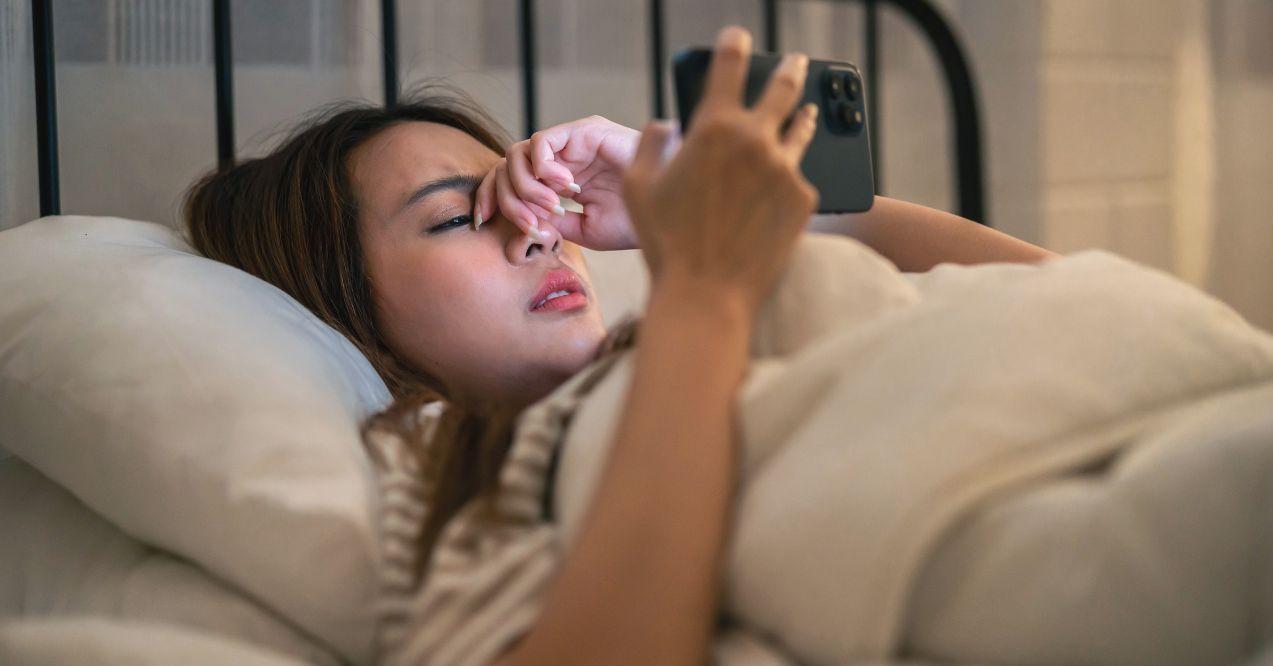 Exhausted Asian young woman hurt eye while using mobile phone at night.