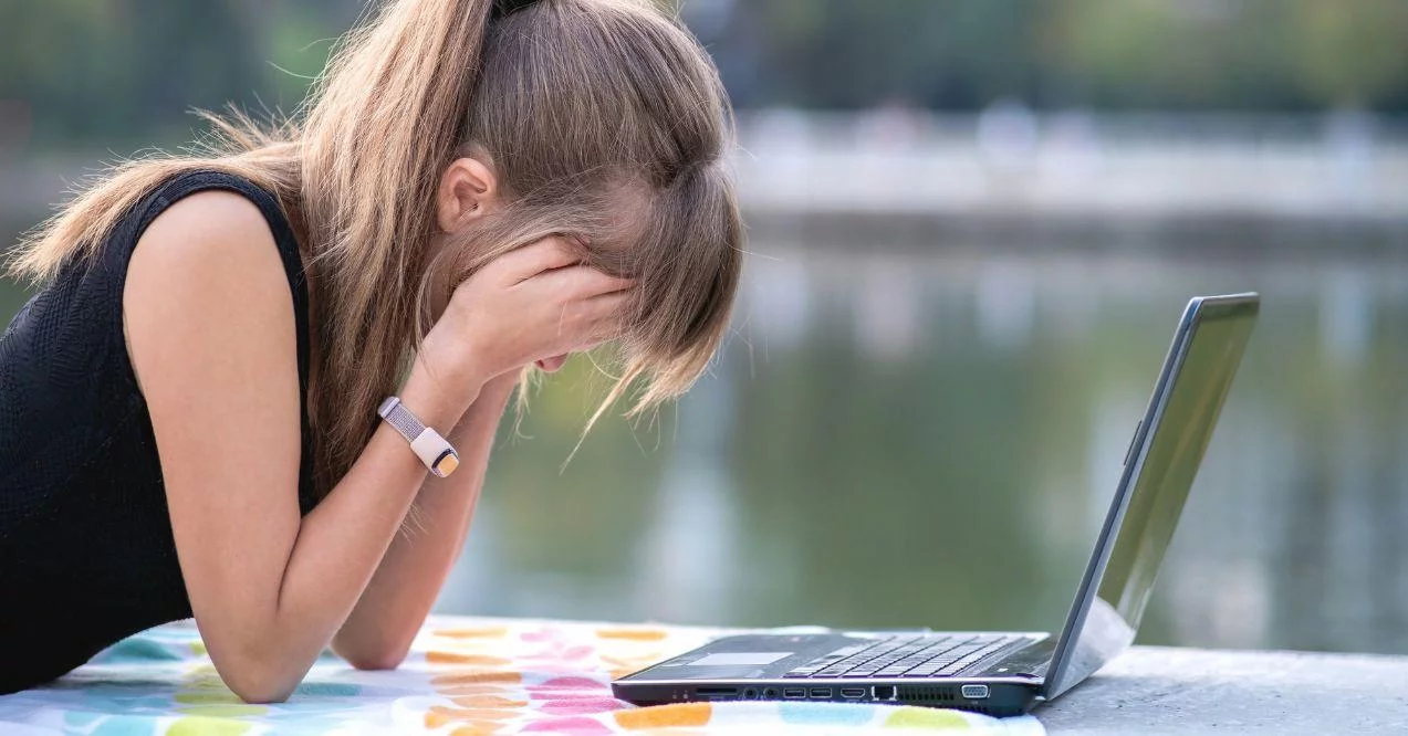 Tired female office employee working behind laptop computer lying down in summer park outdoors