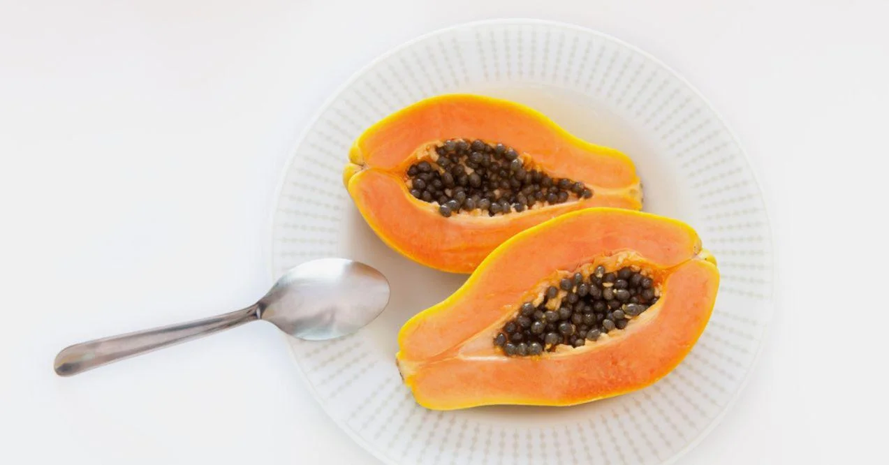 papaya mamao cut in half showing pulp and seeds on white plate on white background with spoon