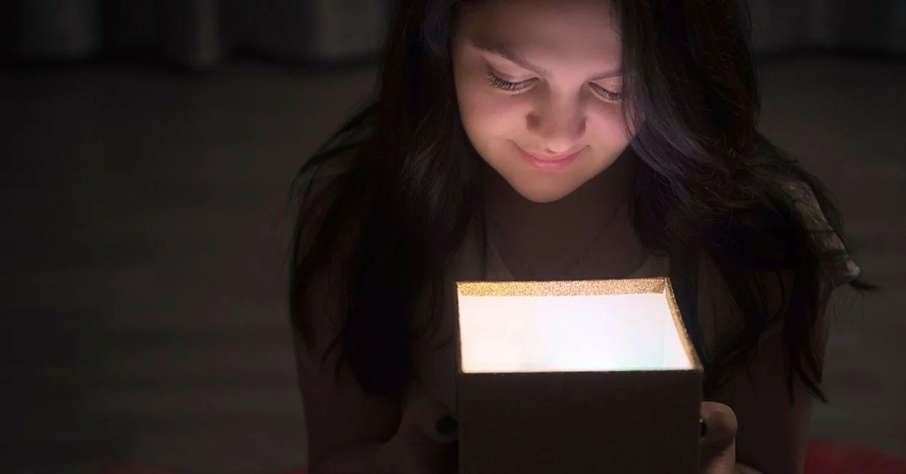 Smiling young brunette girl sitting on the floor and looking into a lamp