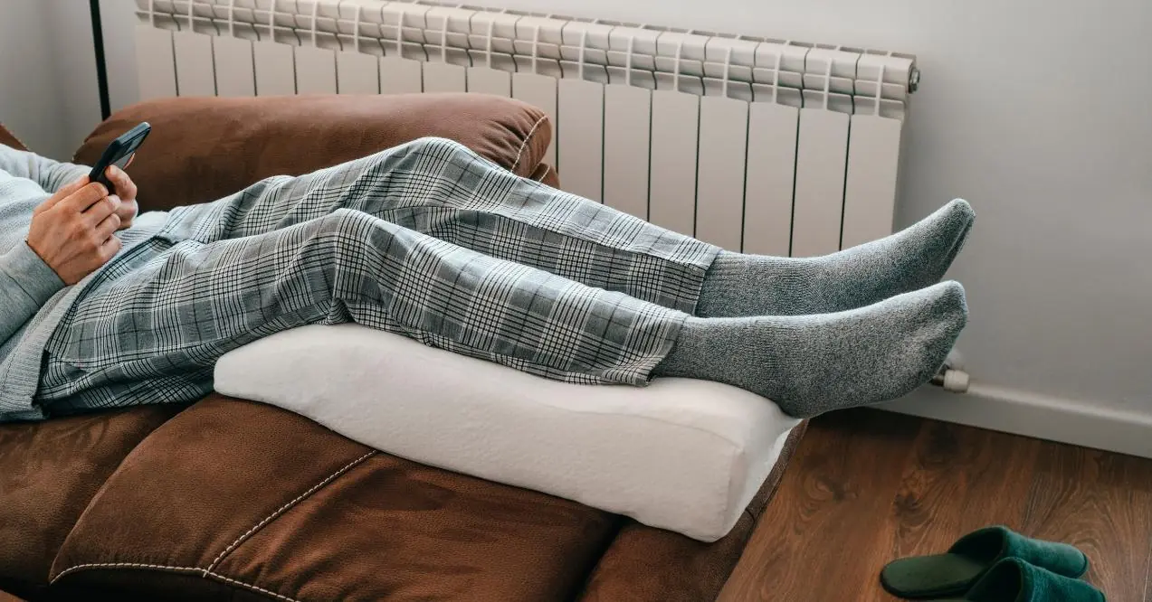 A man leans his legs on a leg elevation pillow