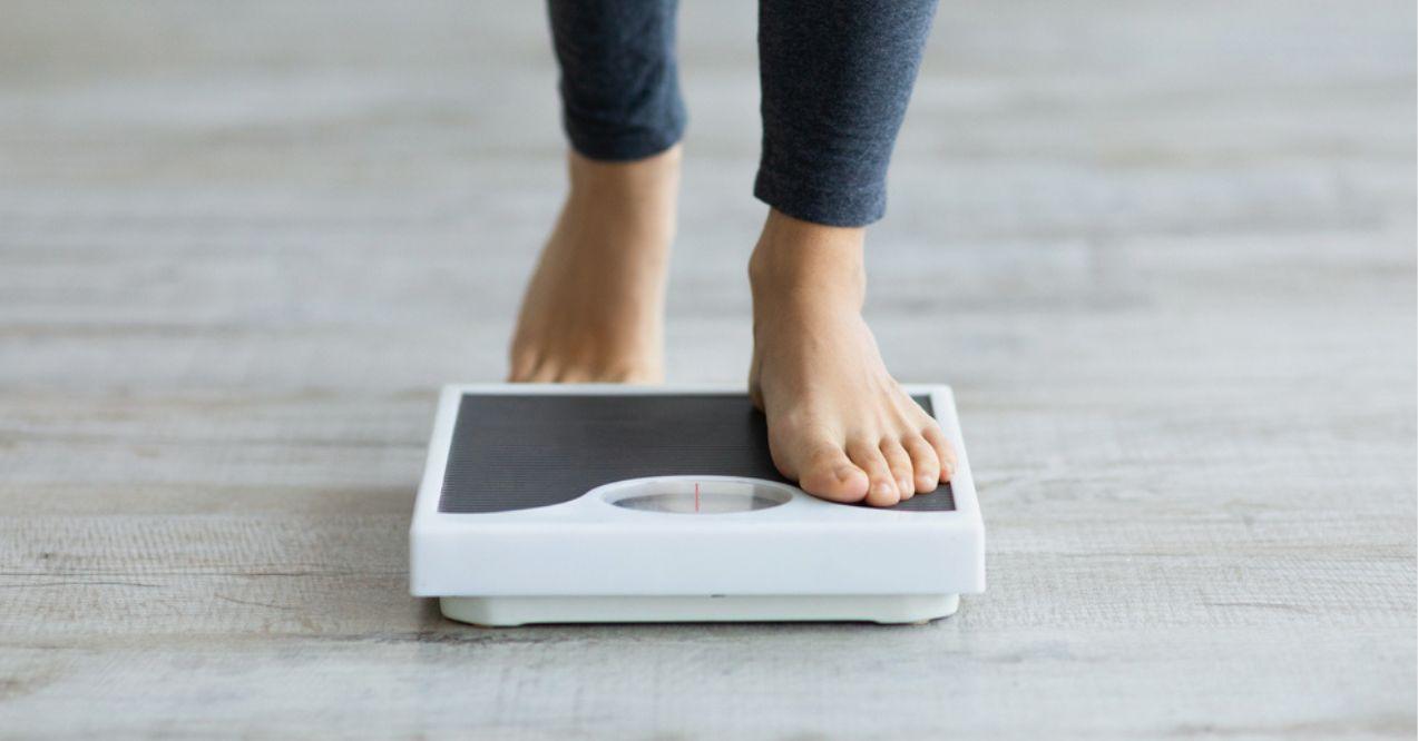 Unrecognizable young woman stepping on scales to measure her weight at home, closeup of feet.