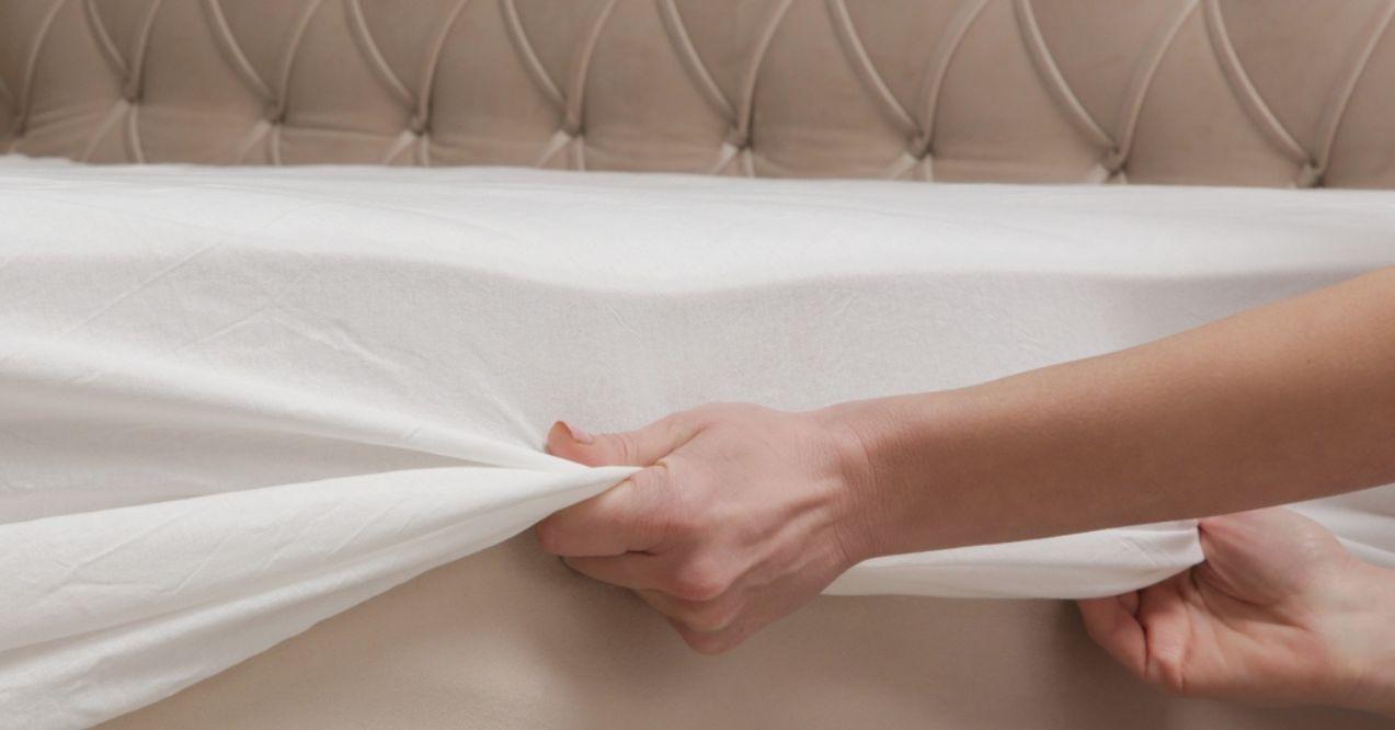 Changing bed sheets. Woman is putting on a fitted white cotton sheet on a mattress while making the bed.