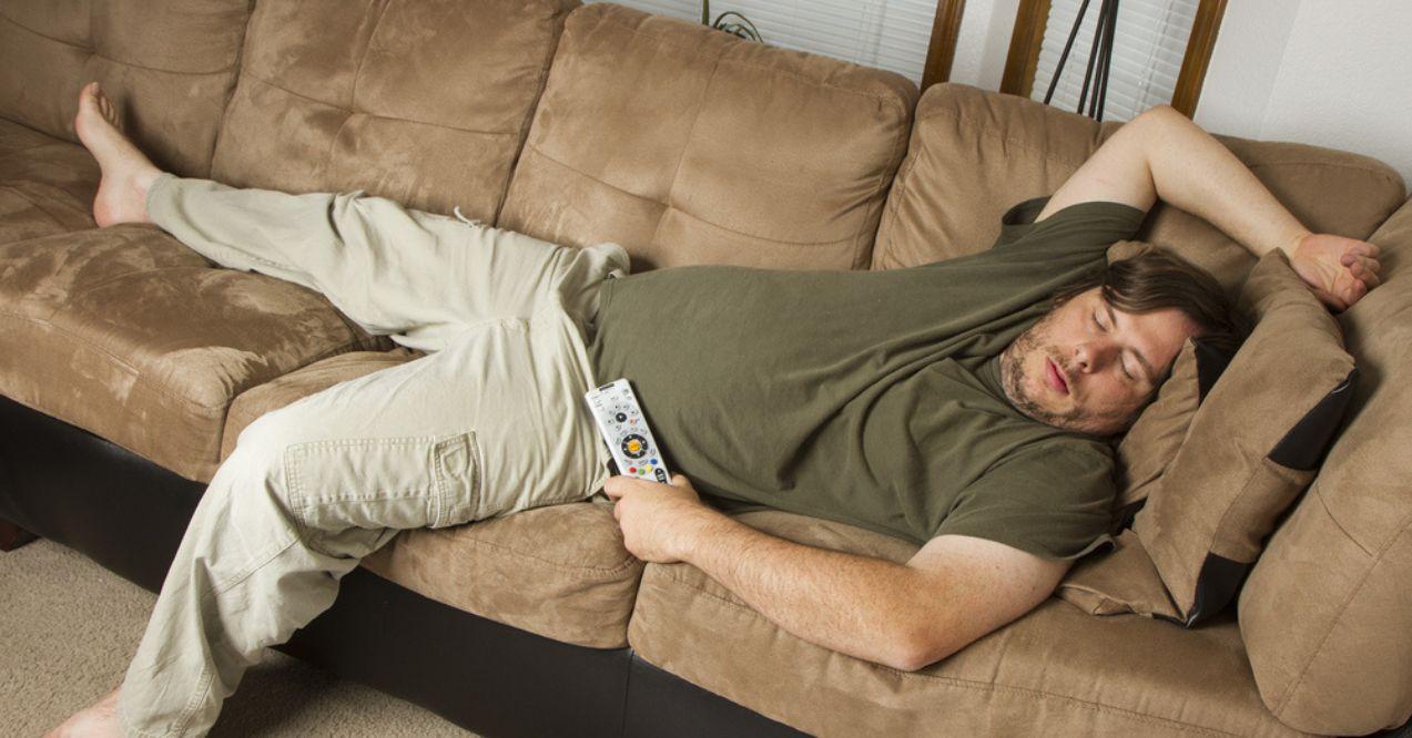 Man sleeping on a sofa with TV remote control in one hand