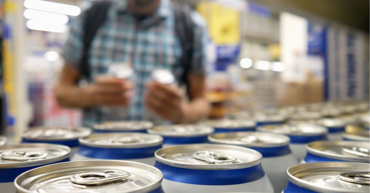 Close-up of many aluminium cans of beer or another drink on a store shelf and a male buyer takes a couple