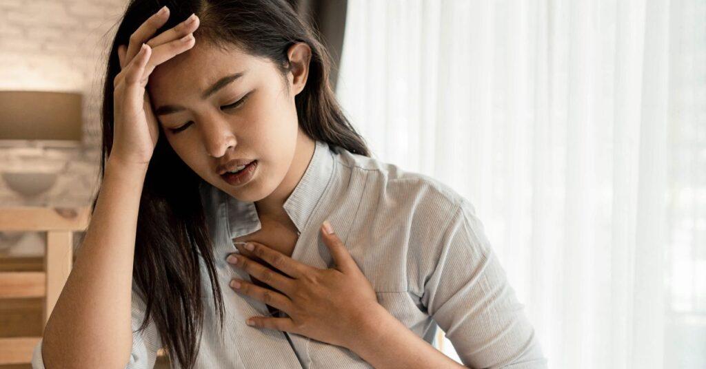 a woman is holding her hand on her head and her other hand on her chest while having breathing problems