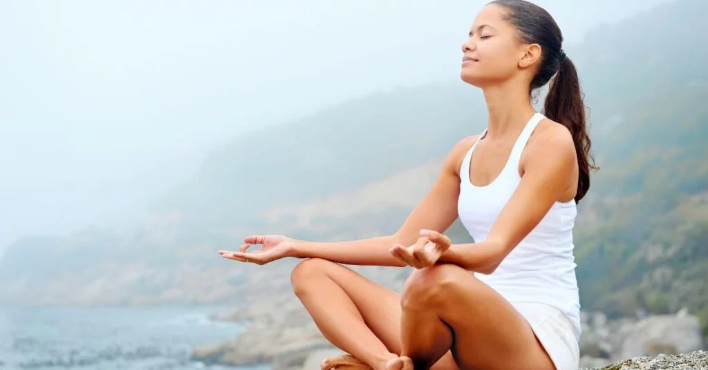 a woman is meditating on a cliff