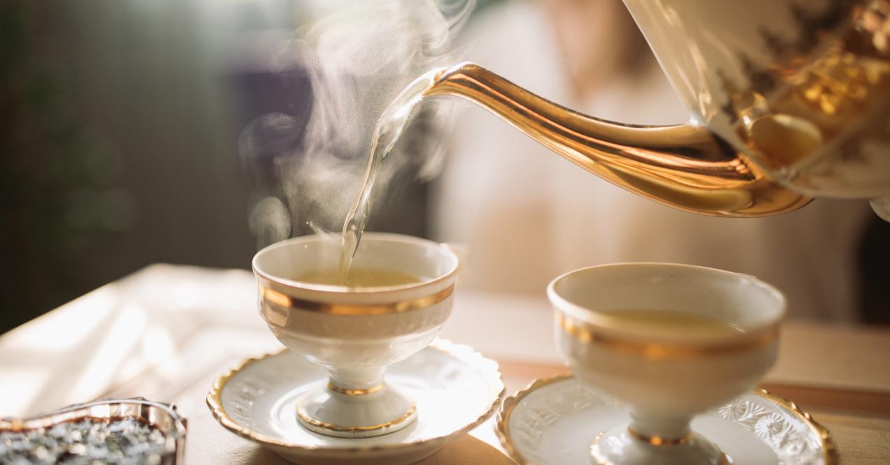 A teapot pouring hot tea into a cup with steam rising