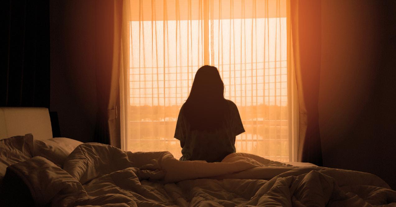 Woman sitting on the bed in the morning with sunlight from the windows