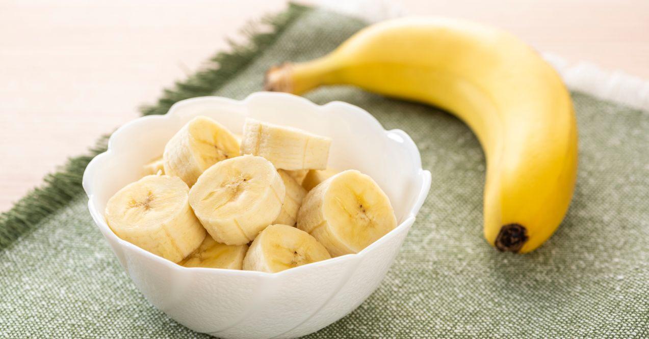 sliced banana in a bowl, with an unpeeled banana on the side
