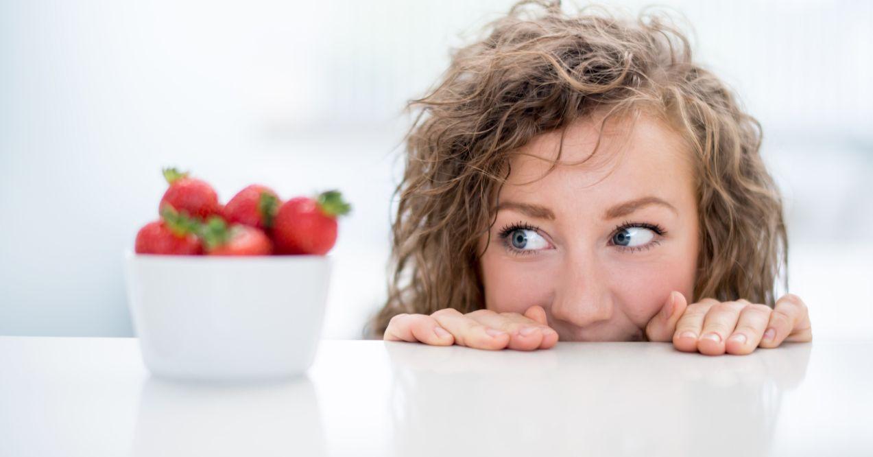 the woman is looking at a bowl of strawberries