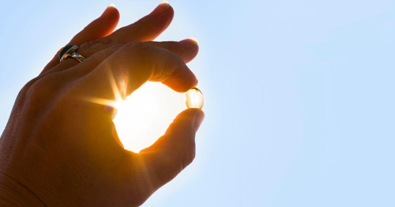 Vitamin D capsule being held up high next to the sun